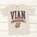 A cream-colored short-sleeve t-shirt with a distressed graphic reading 'VIAN WOLVERINES' in purple and gold, featuring a wolverine mascot with his claw wrapped around the Vian victory V logo.